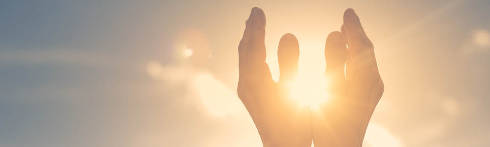 Close-up of hands up in prayer around the sun Close-up of hands up in prayer around the sun